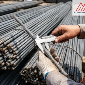 Petugas proyek mengukur diameter batang besi beton ulir menggunakan jangka sorong di depan tumpukan besi beton