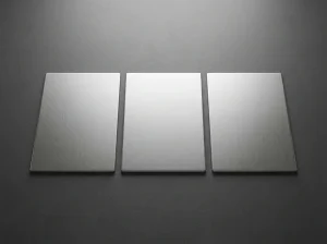 Tiga potongan pelat stainless steel dengan permukaan brushed disusun berdampingan di atas permukaan gelap